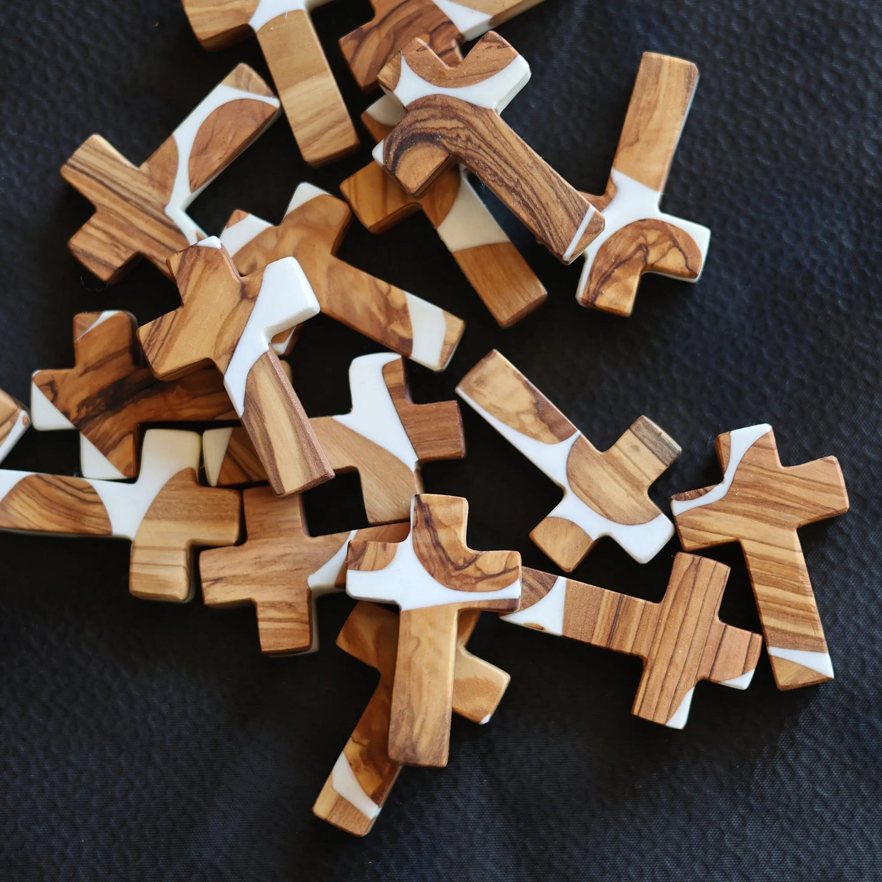 Olive wood crosses with white resin in a pile on a black surface.