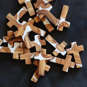 Olive wood crosses with white resin in a pile on a black surface.