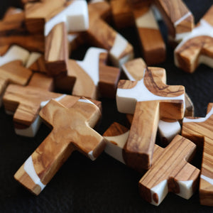 Pile of wooden pocket crosses with white resin inserts and natural grain.