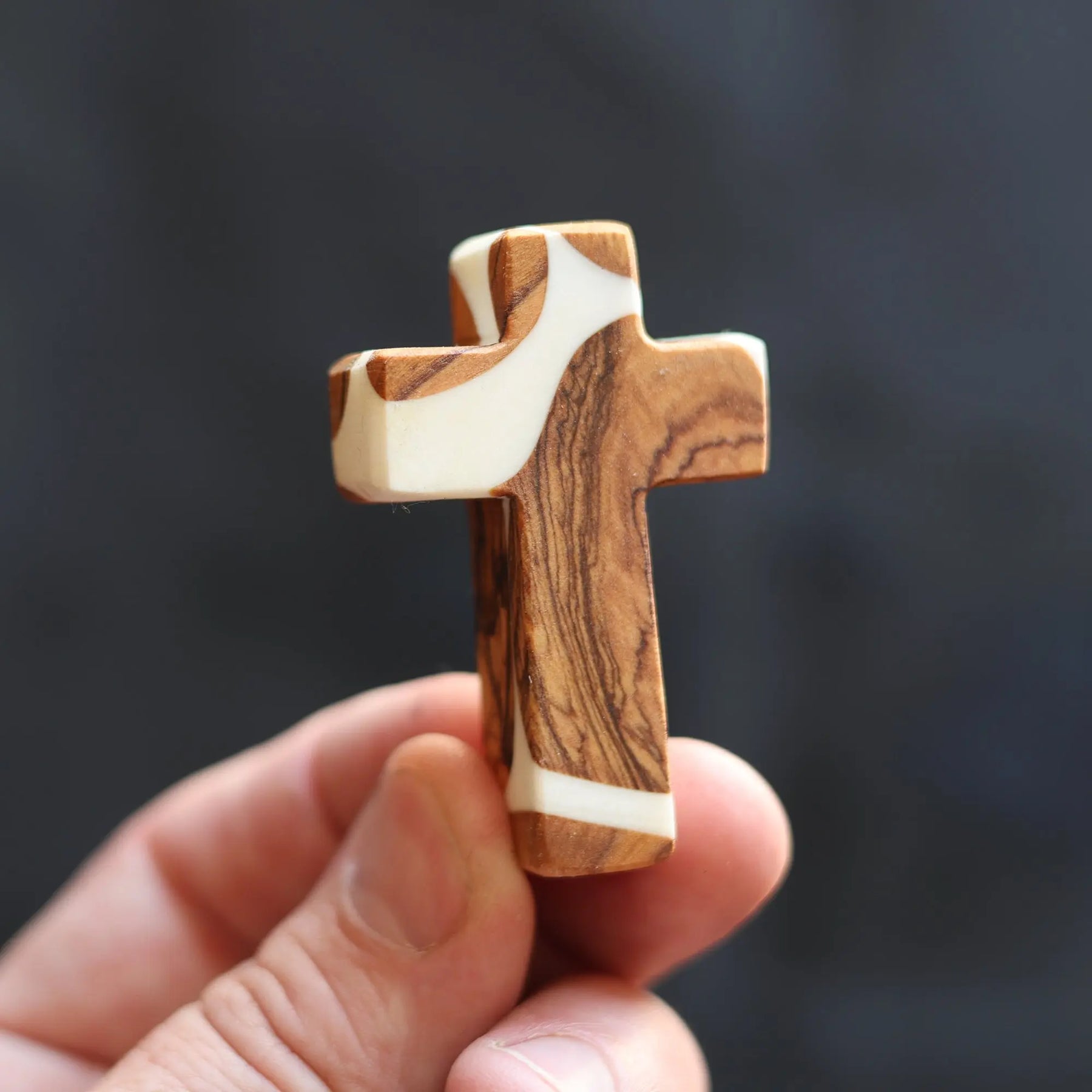 Olive wood and white resin pocket cross held by a hand.