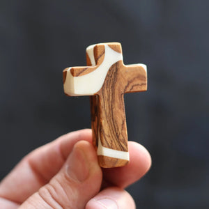 Olive wood and white resin pocket cross held by a hand.