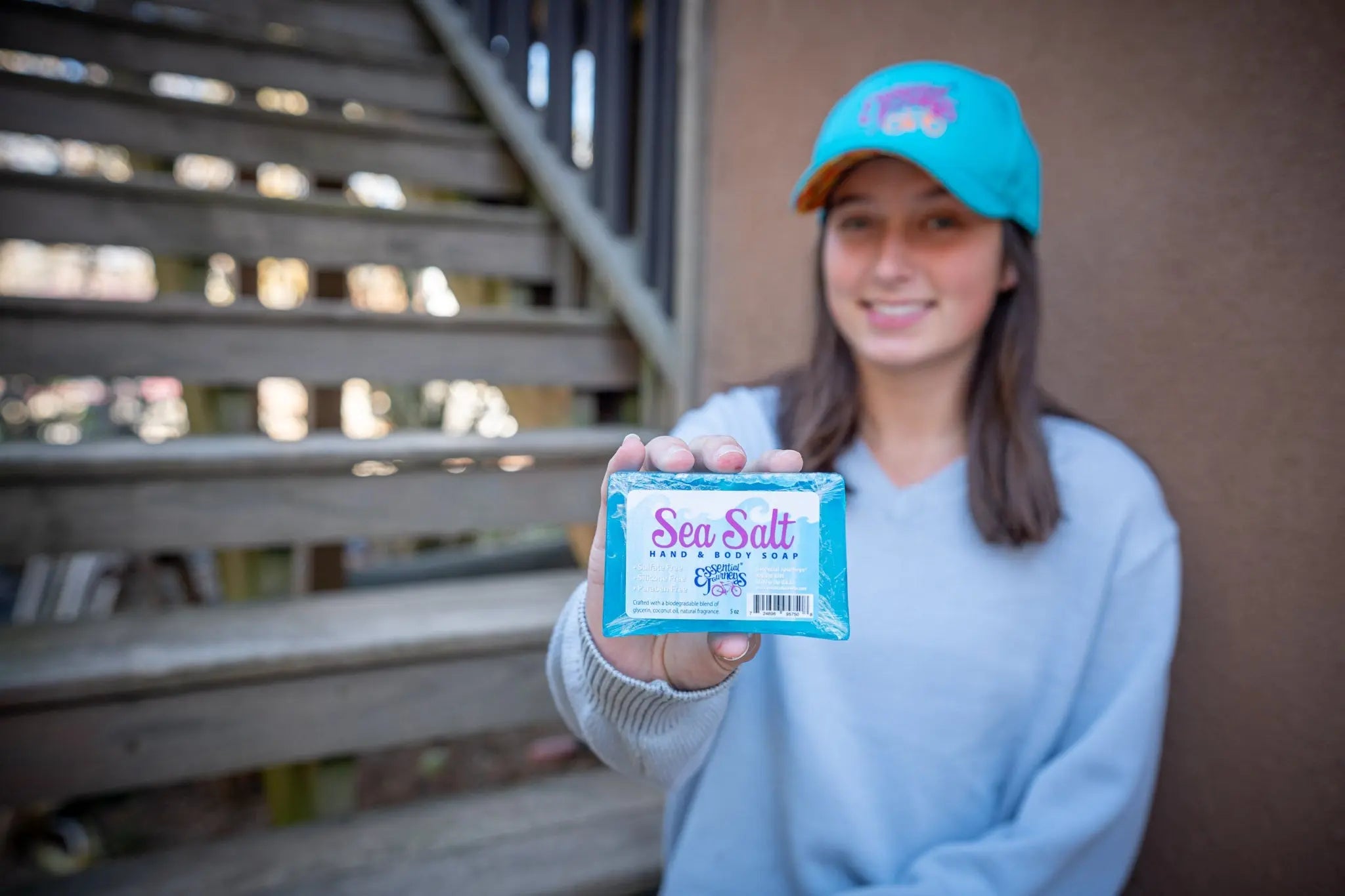Woman in blue sweatshirt and cap holds sea salt hand and body soap bar.