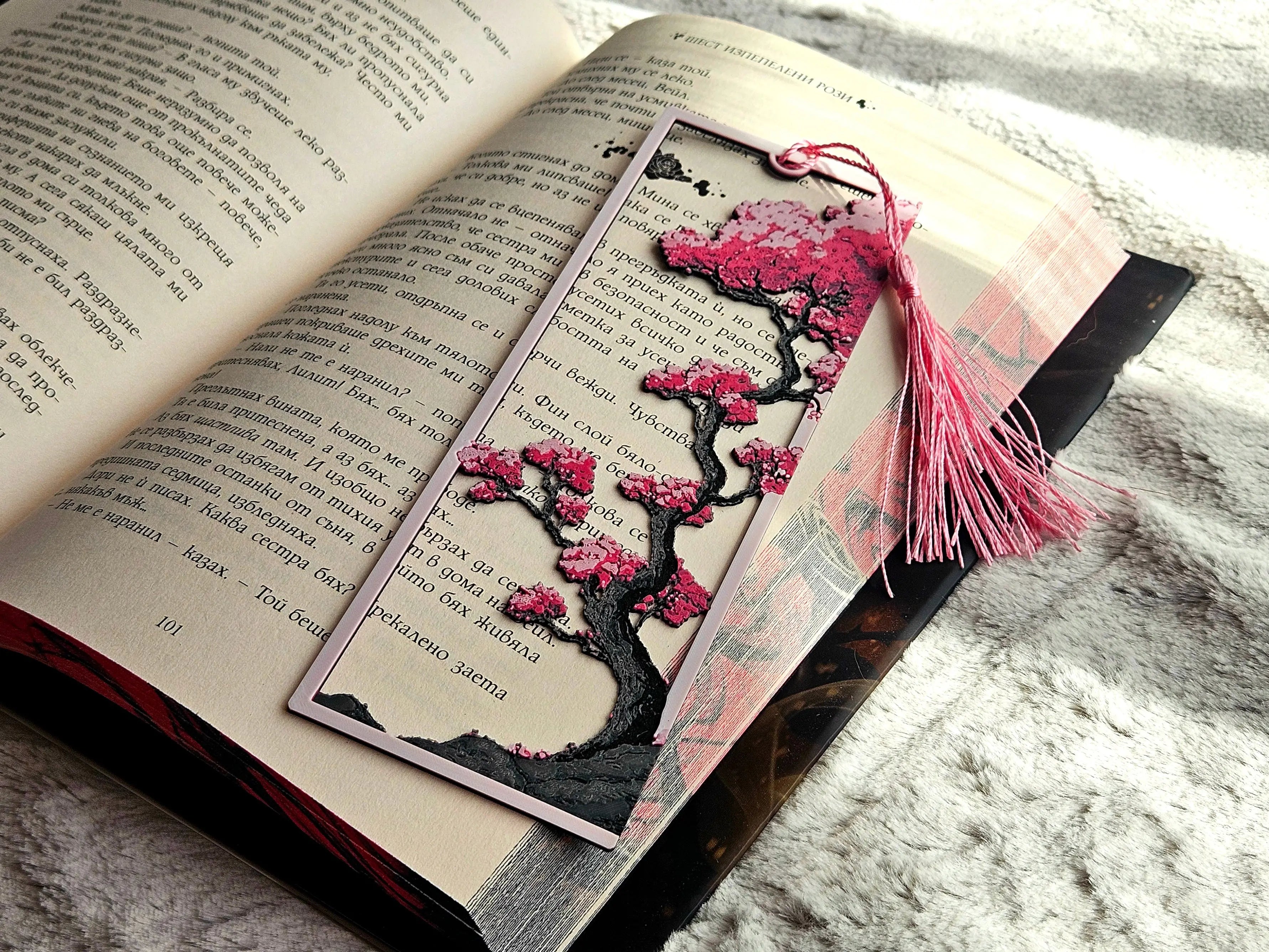 Bookmark with a sakura tree and samurai design; pink tassel. Book open to page 101.