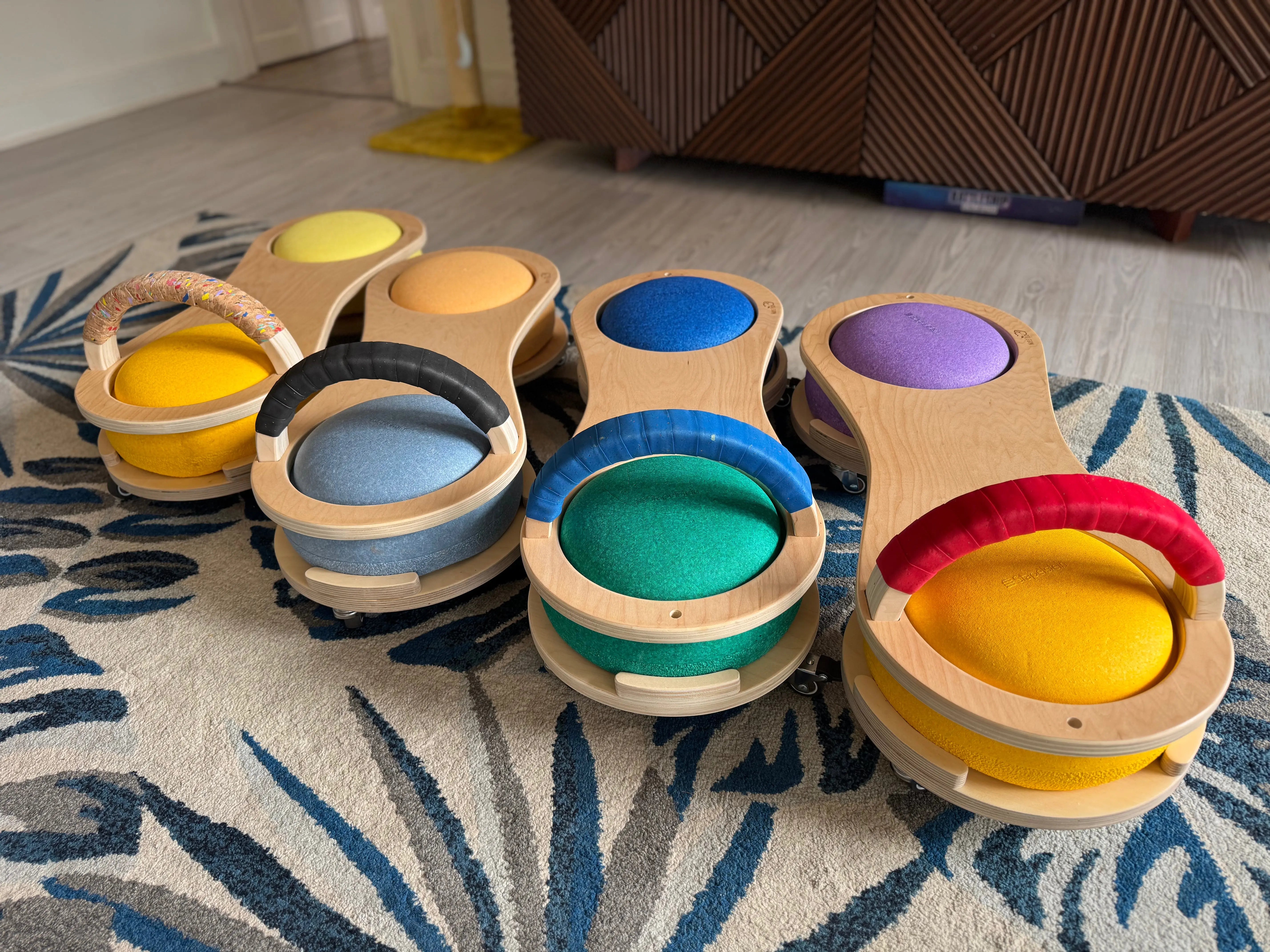 Wooden scooter boards with colorful seats on a rug.