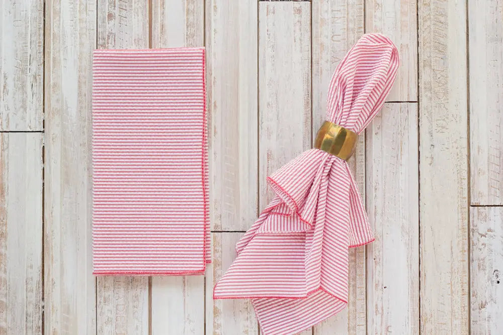 Red and white striped seersucker napkins folded with a gold napkin ring.