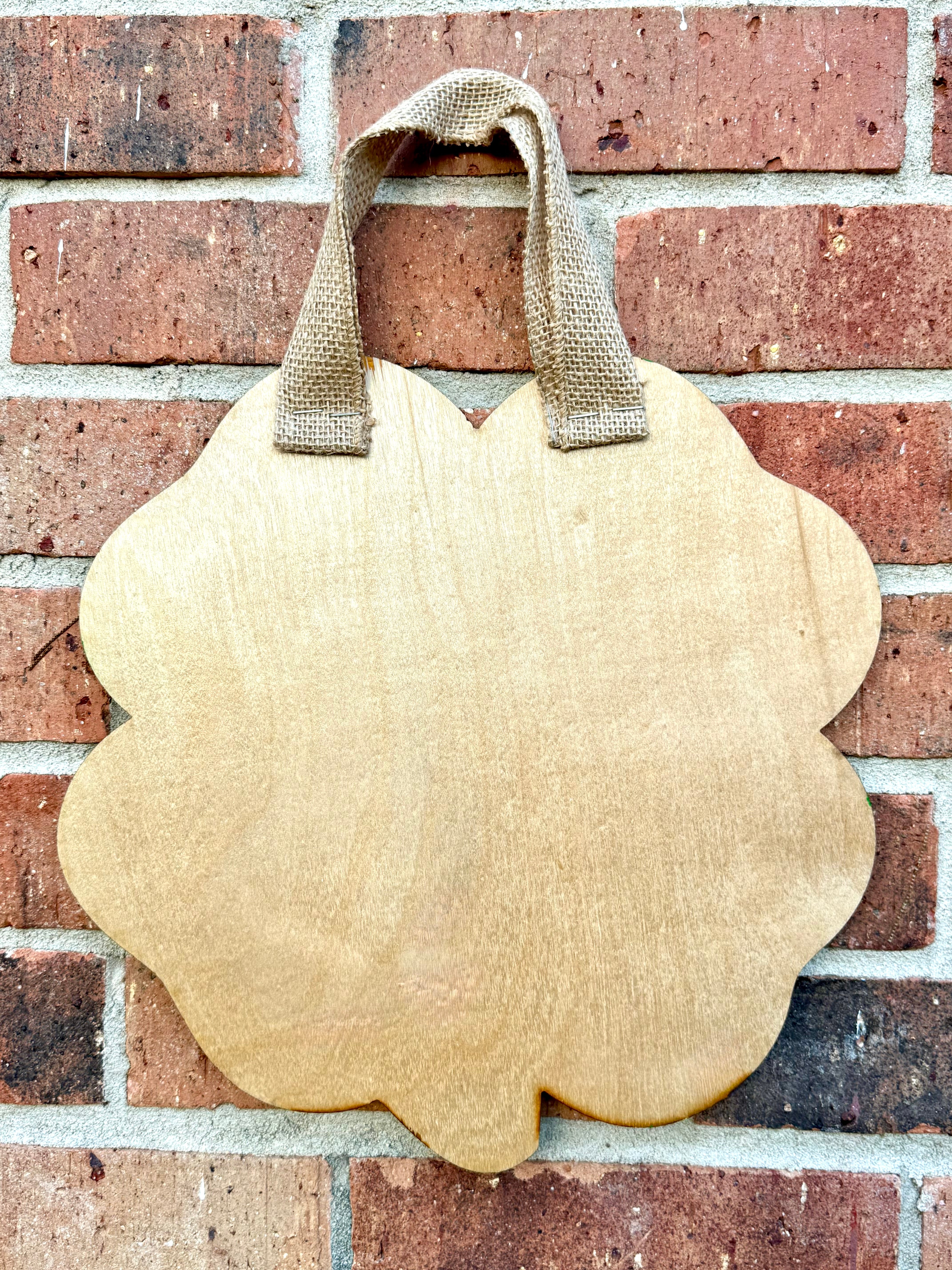 Shamrock door hanger, wooden with burlap ribbon, hanging on red brick wall. St. Patrick's Day decoration.