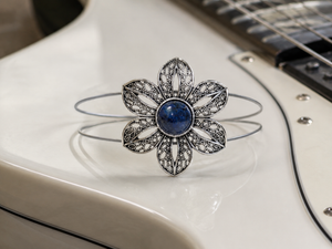 Silver flower-shaped brooch with a blue gemstone on a white surface
