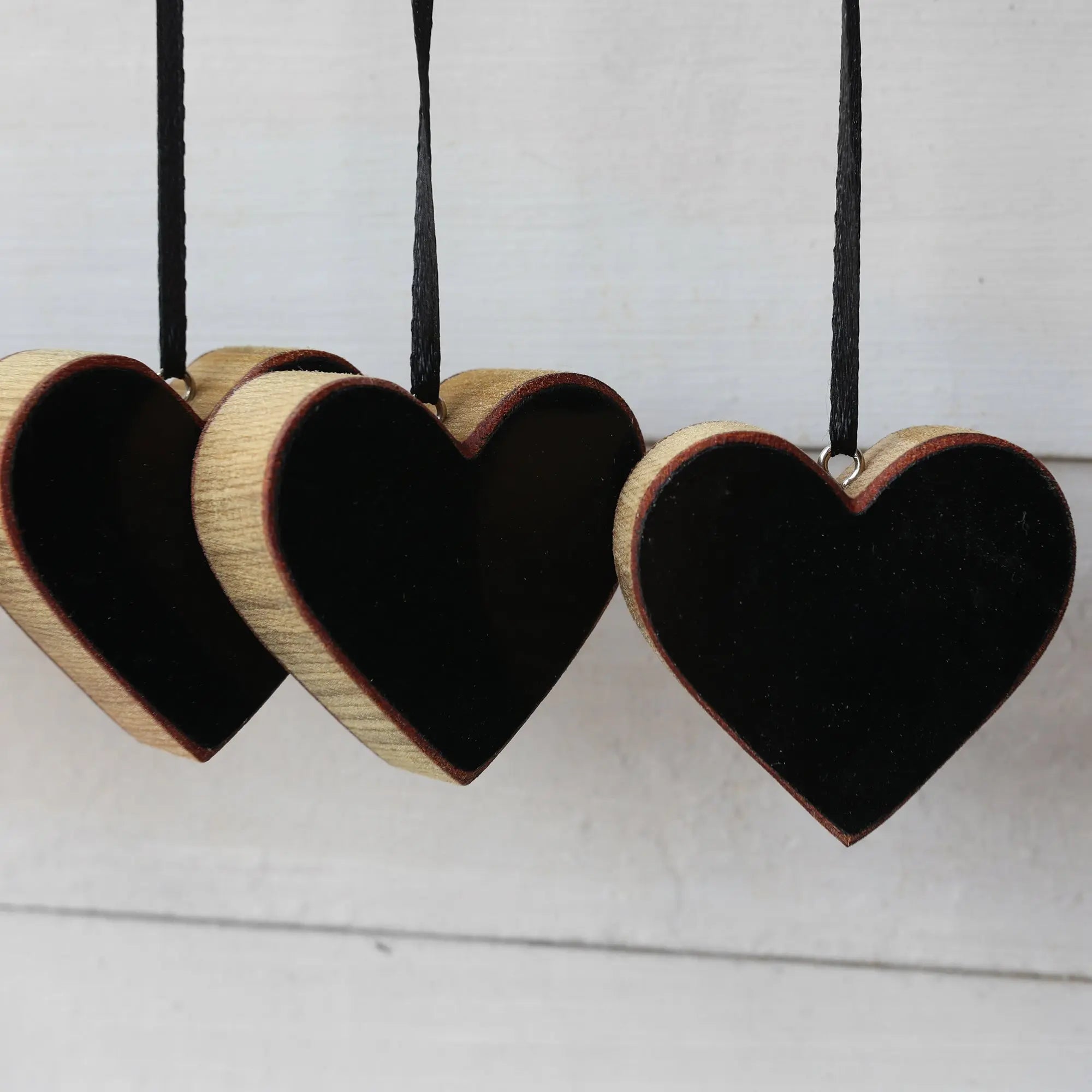 Three wooden heart ornaments with black centers, hanging by black ribbons.