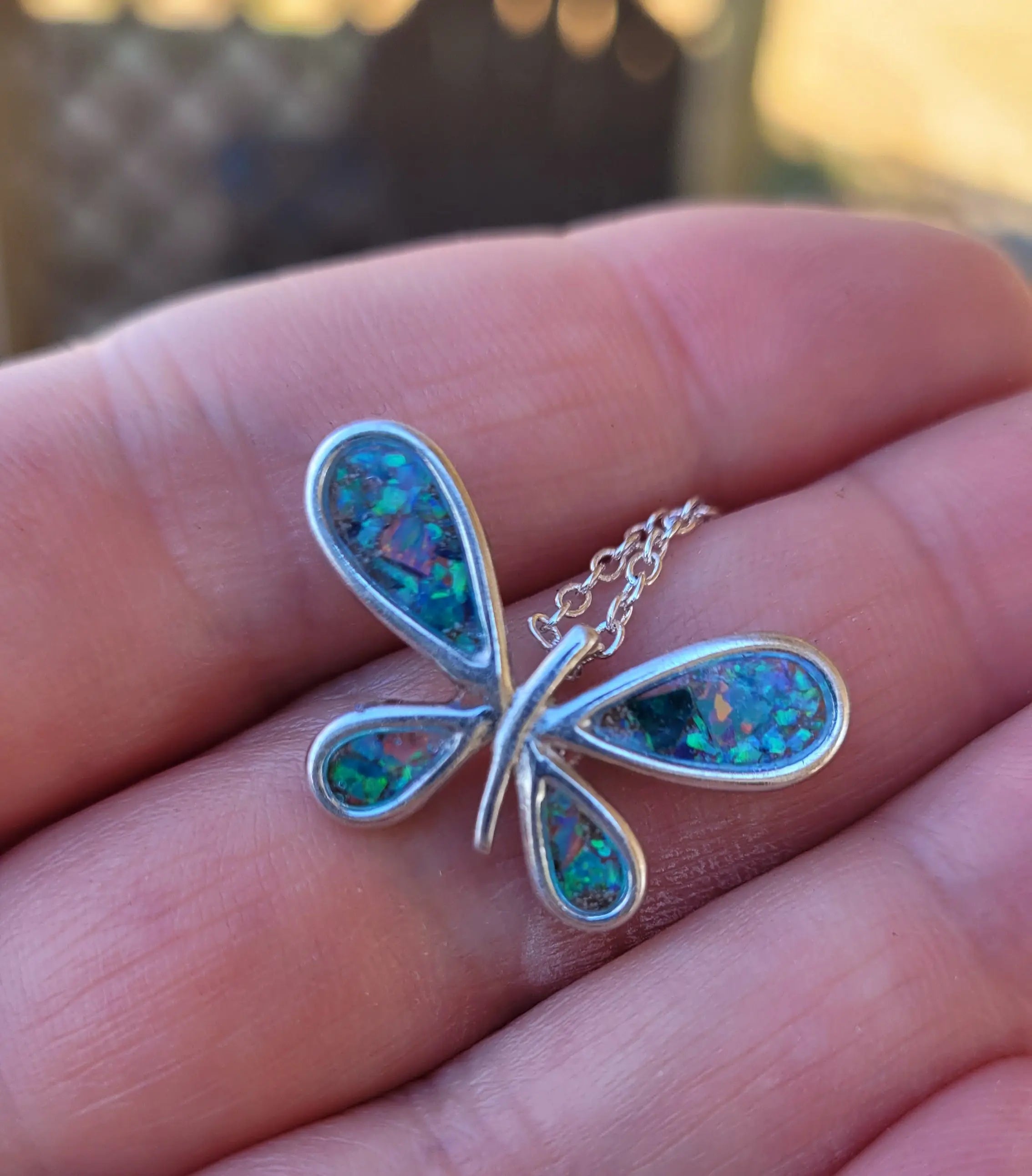 Sterling silver butterfly pendant necklace with colorful stone inlay in hand.