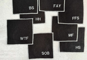 Black linen cocktail coasters with white embroidered letters.