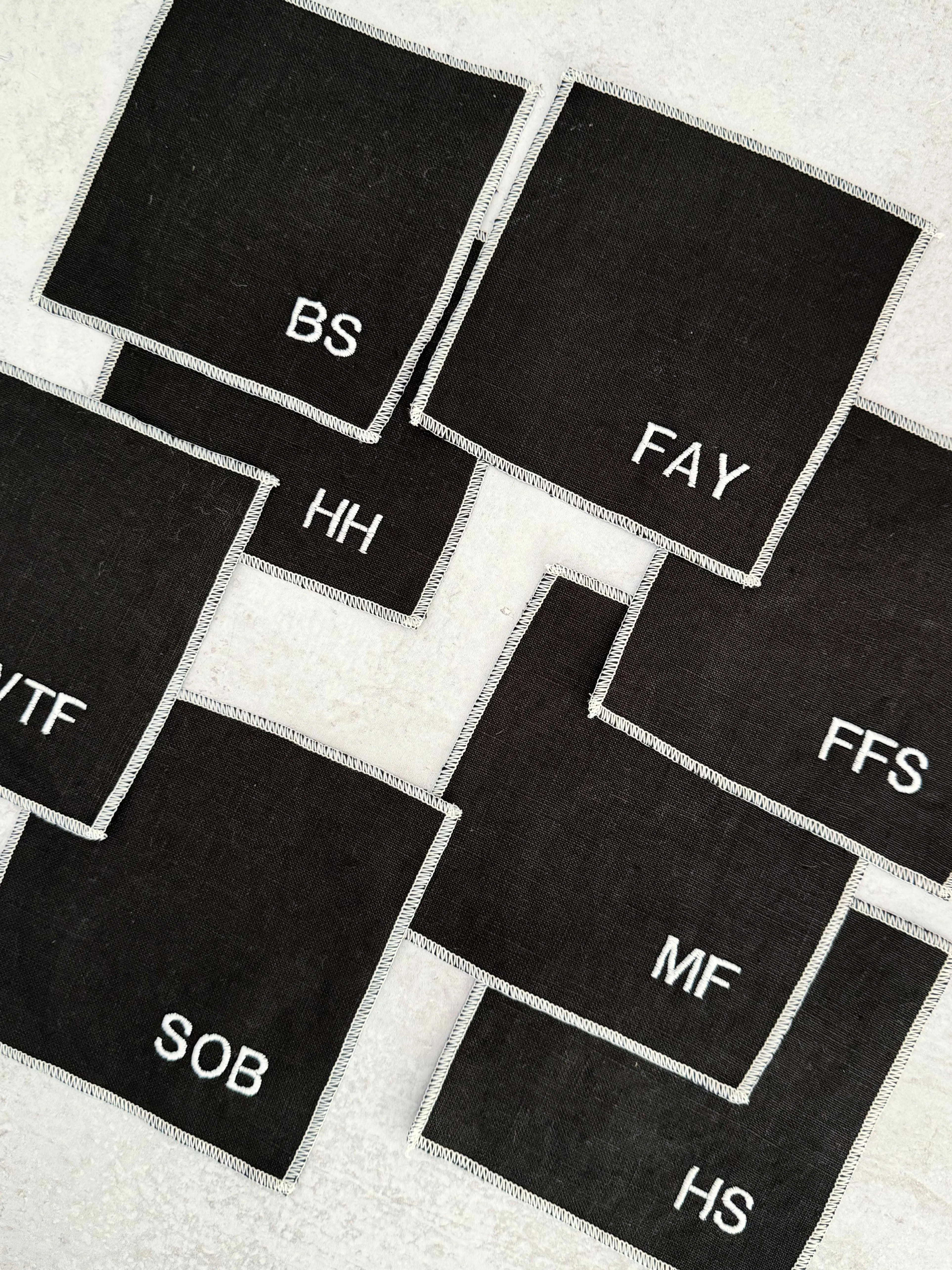 Black linen coasters with white embroidered initials arranged on a surface.