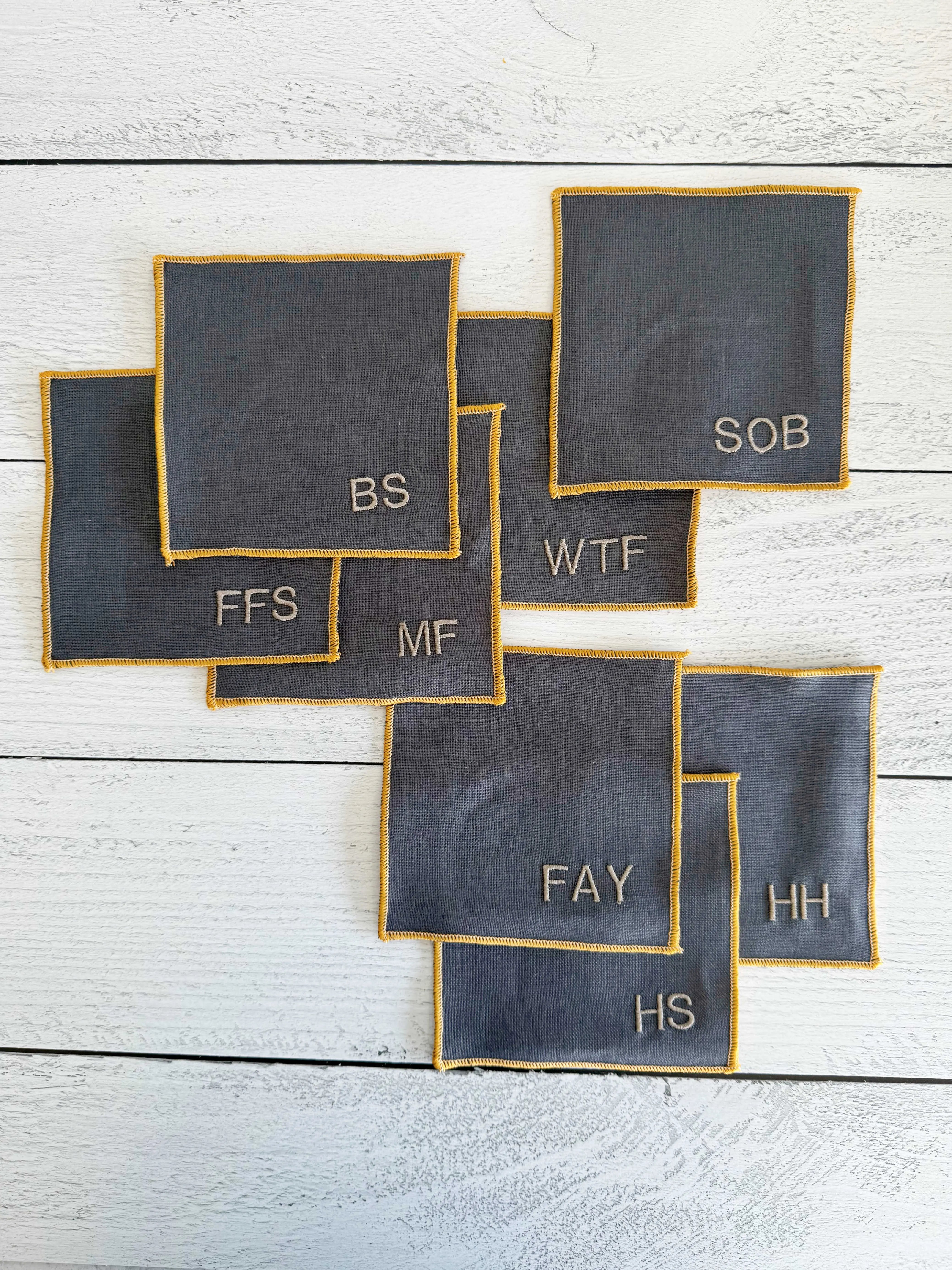 Grey linen coasters with embroidered monograms and yellow trim.