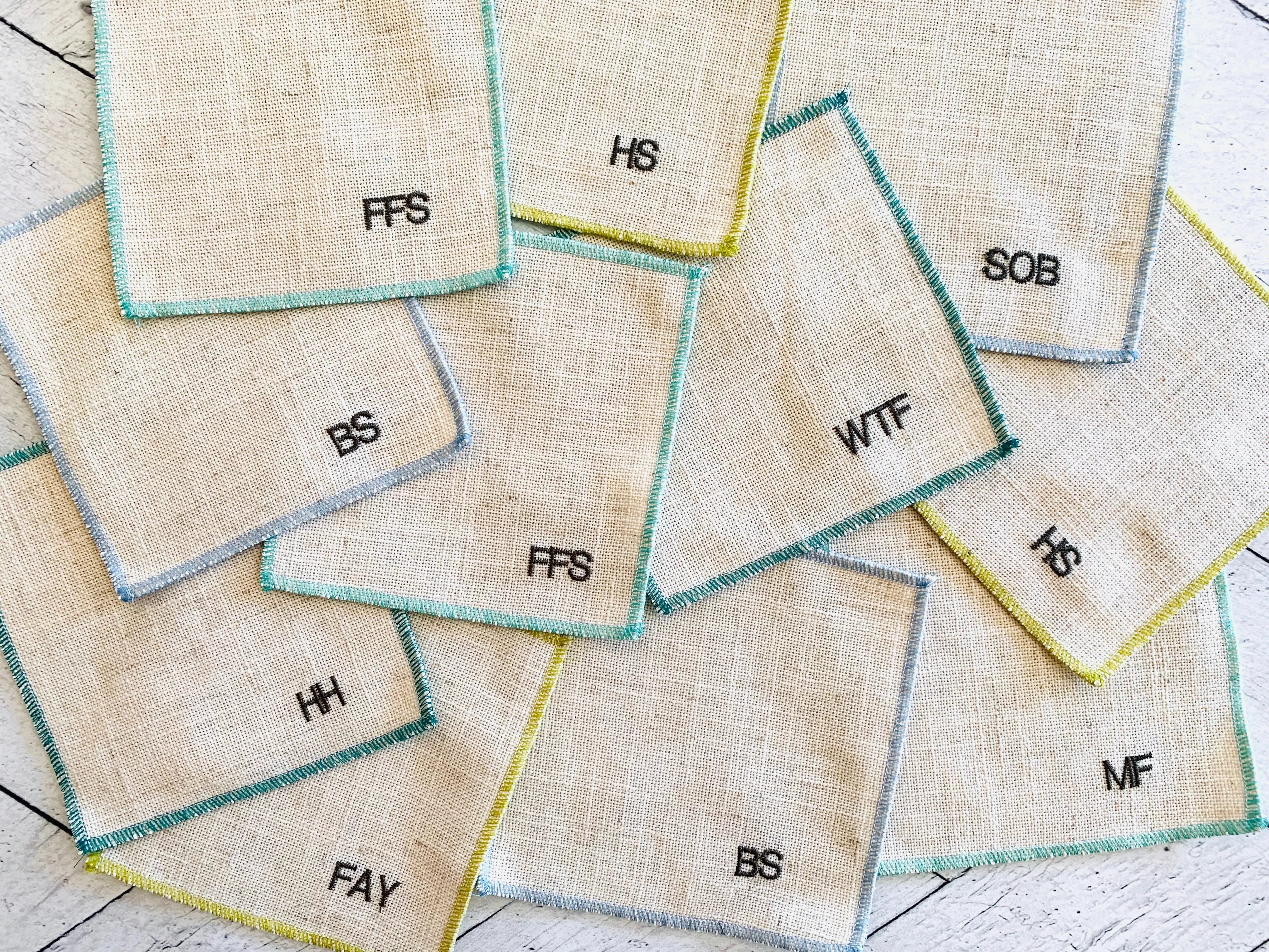 Set of 8 sweary cocktail coasters with embroidered letters on linen fabric.