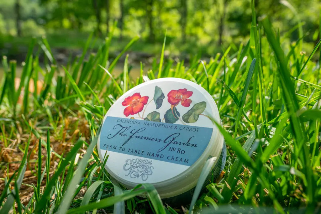 Round container of "The Farmers Garden" hand cream with floral illustrations, nestled in grass.