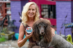Woman holding a jar of Farmers Garden hand cream next to a standard poodle dog.