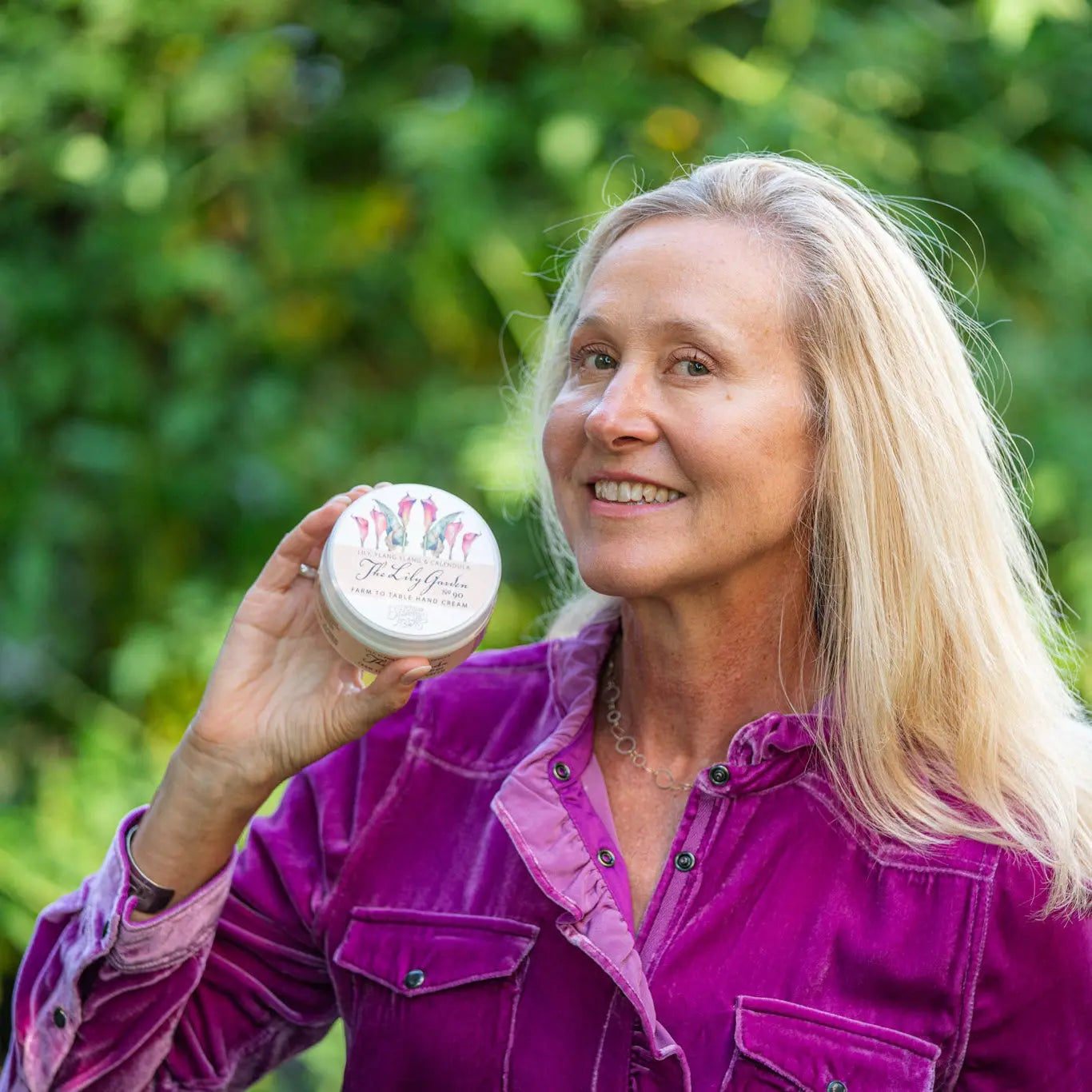 Woman holding a jar of The Lily Garden Farm to Table Hand Cream with floral label.