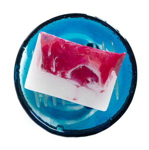 Pink and white marbled goat's milk soap slice on a blue soap dish.