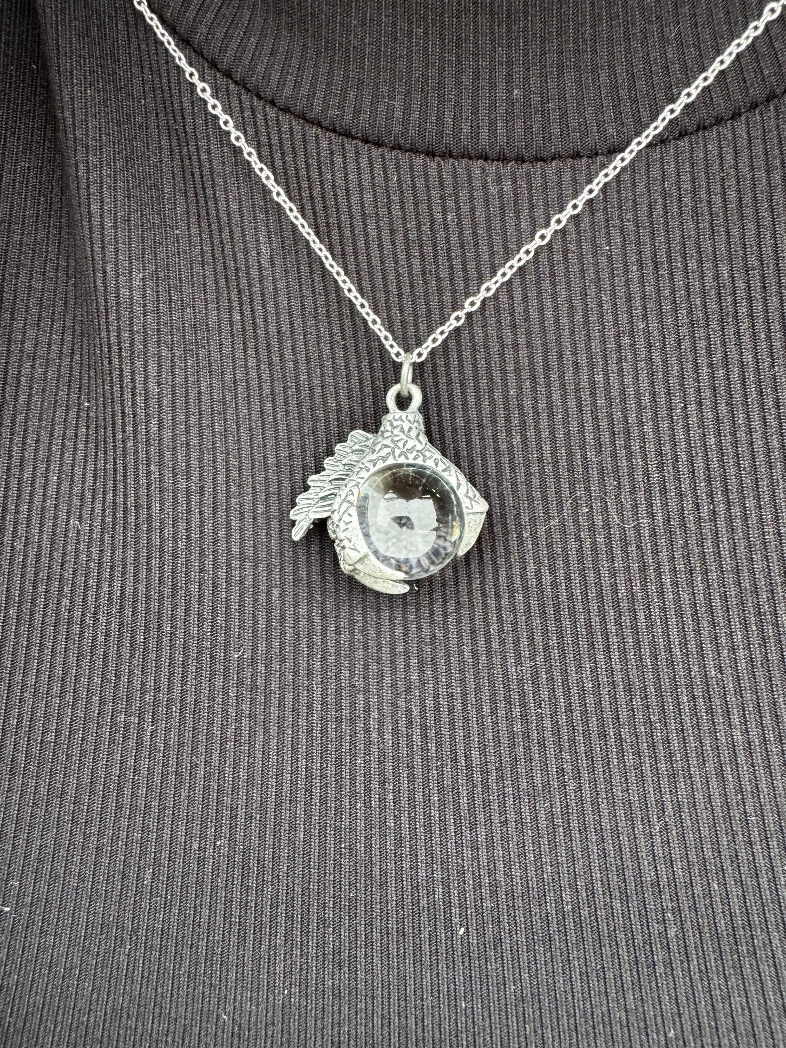 Silver-tone dragon claw necklace with a glass orb pendant on a chain.
