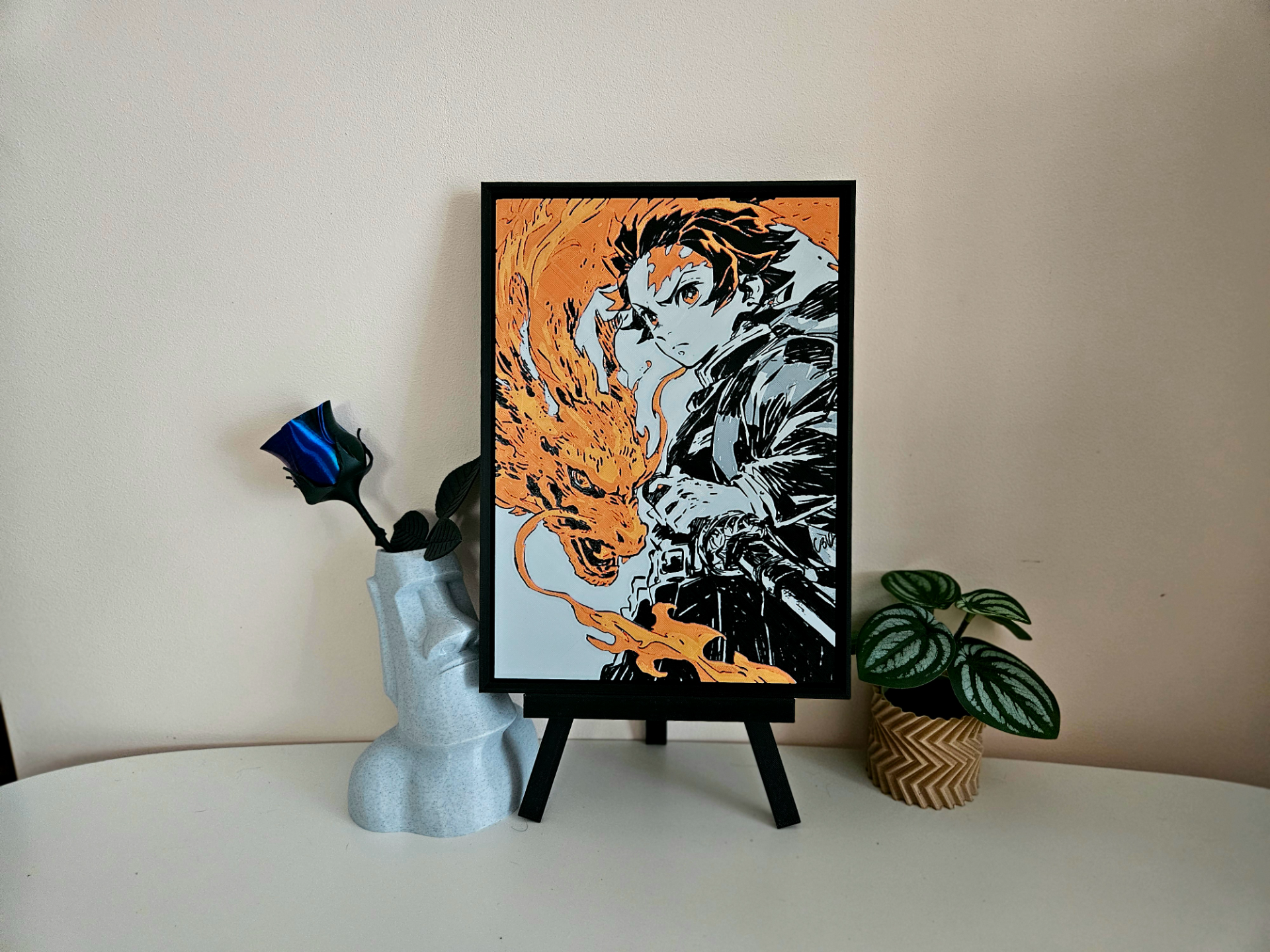 Demon Slayer filament painting of Tanjiro with Hinokami Kagura flames on a black easel with a plant and vase.