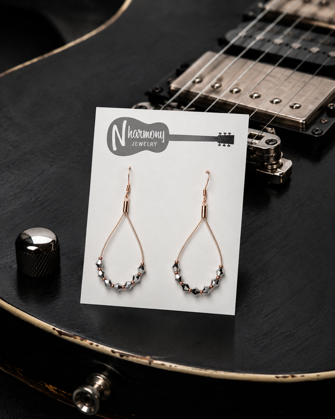 Pair of earrings on a Harmony Jewelry card with a guitar in the background