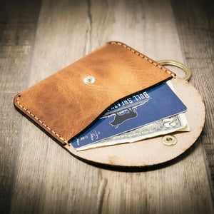 Brown leather keychain wallet with a snap, holding an ID card and dollar bills.