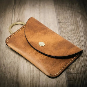 Brown leather keychain wallet with a brass snap closure and keyring on a wooden background.