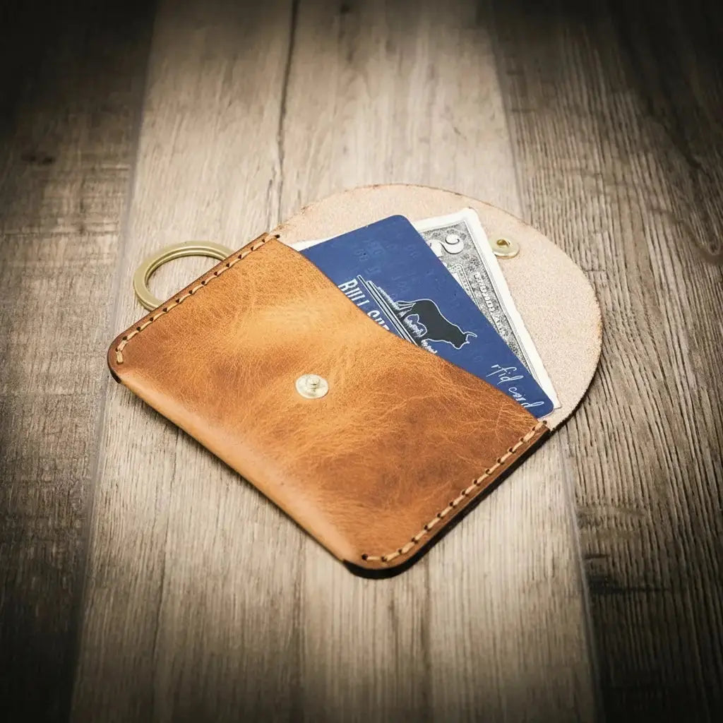 Brown leather keychain wallet with snap closure holding credit cards and a bill.