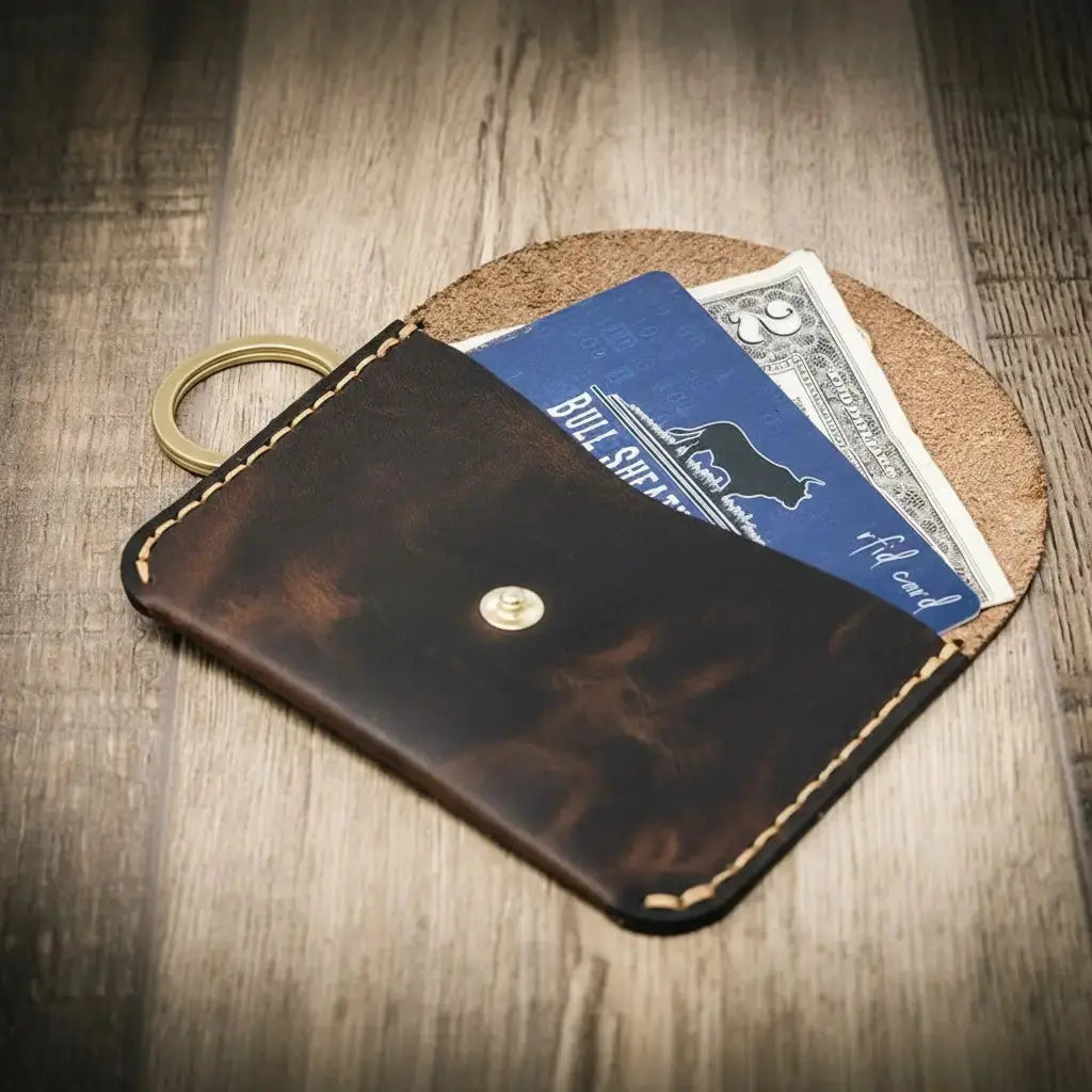 Brown leather keychain wallet holding cards and folded cash with a brass keyring.