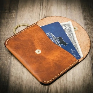 Brown leather keychain wallet holding a blue card and a bill.
