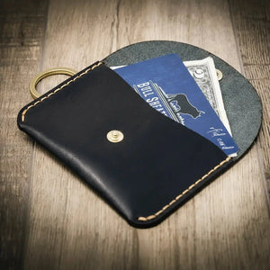 Dark blue leather keychain wallet holding cards and cash on a wooden surface.