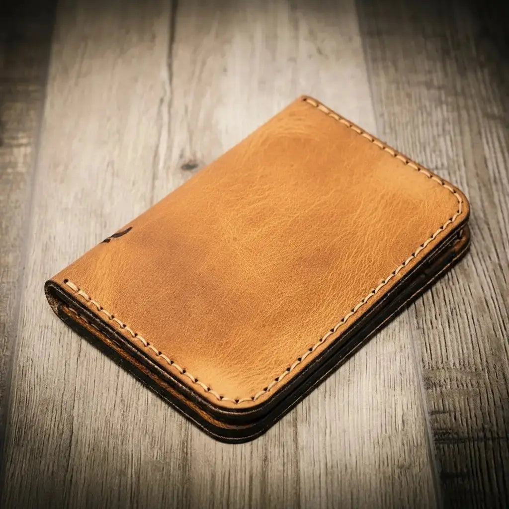 Brown full grain leather vertical wallet with stitched edges on a wood background.