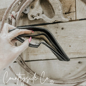 Hand holding a black leather wallet with cash inside, showing lining with "Countryside Co." logo.