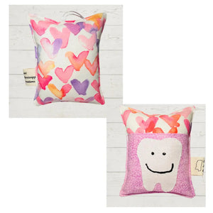 Two tooth fairy pillows, one with heart pattern and one with a tooth face on a pink floral fabric.