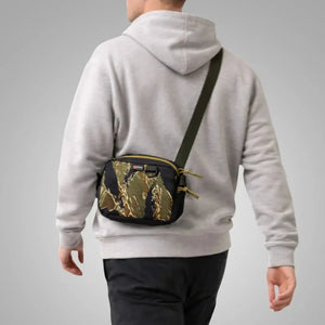 Man wearing a camouflage fanny pack crossbody over a grey hoodie.