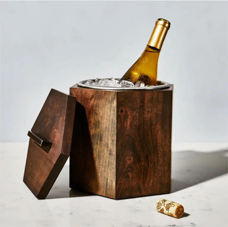 Wooden ice bucket with open lid, filled with ice and a wine bottle; a cork sits on the marble surface.