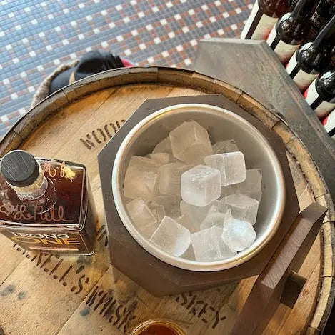 Wooden ice bucket on a whiskey barrel featuring ice cubes and a bottle of Irons One Total Nell's whiskey.