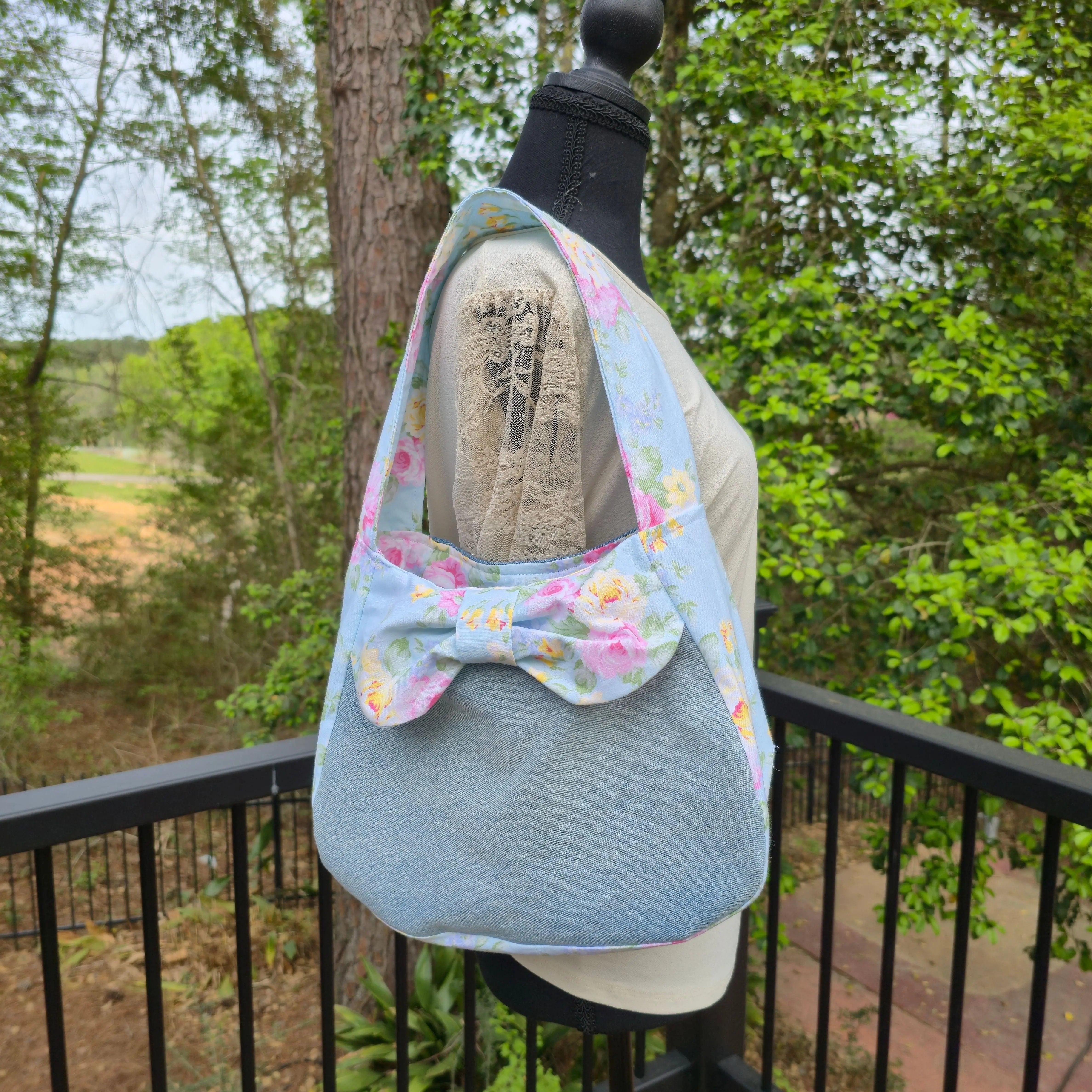 Blue denim shoulder bag with a light blue floral fabric bow detail.