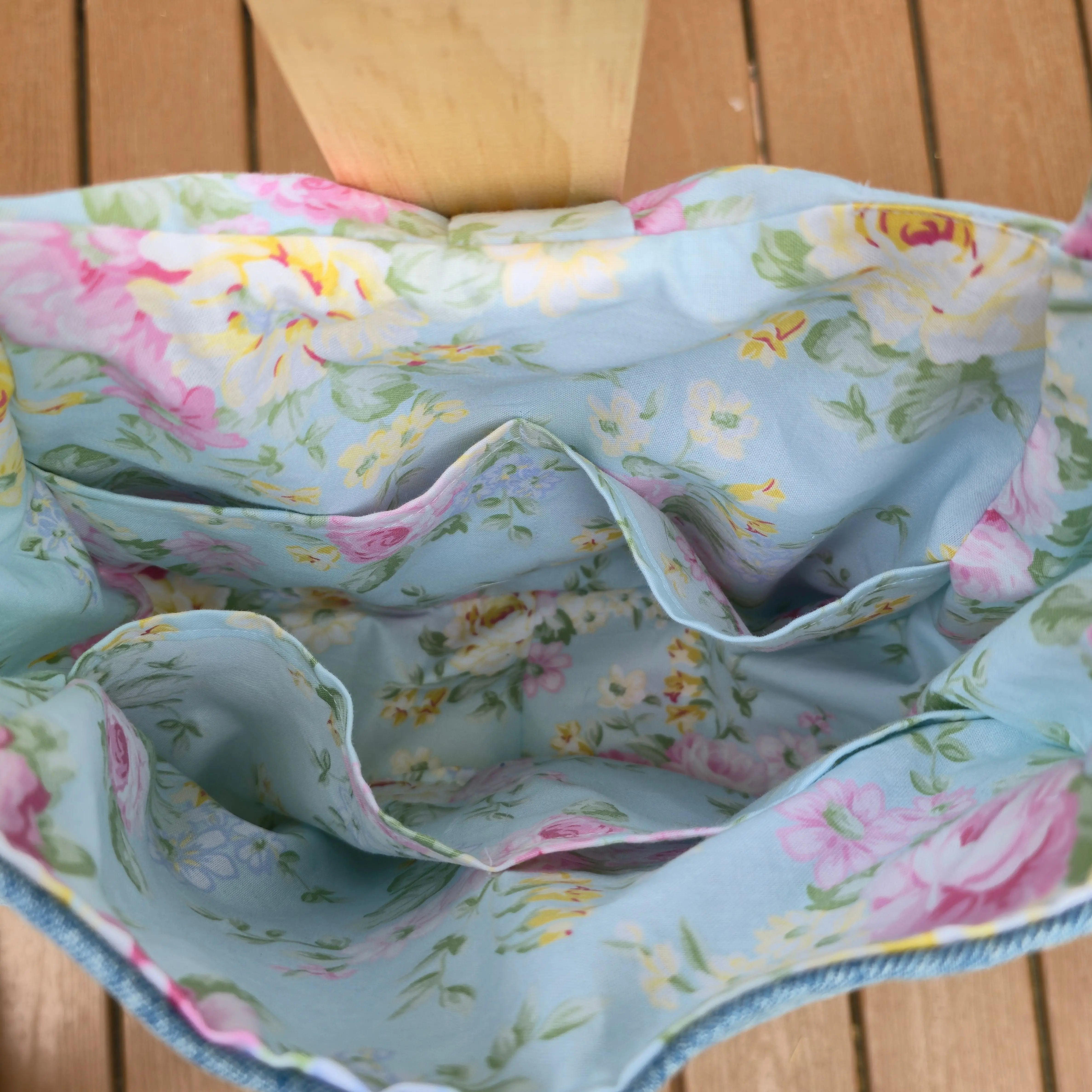 Denim shoulder bag with light blue floral lining and interior pockets.