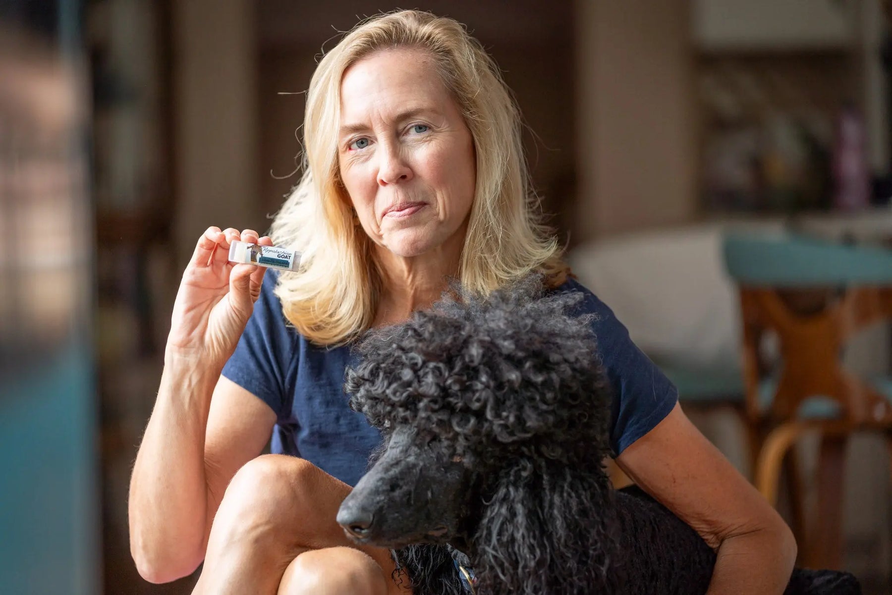 Woman holding a Vanilla Swirl lip balm tube next to a black poodle.