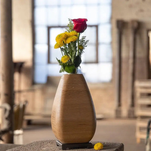 White oak wooden vase with a bronze base holding a red rose and yellow flowers.