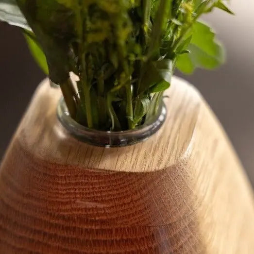 Wooden vase with greenery, bronze base. Cylinder glass insert holds plant stems and water. Salvaged urban wood is laminated.