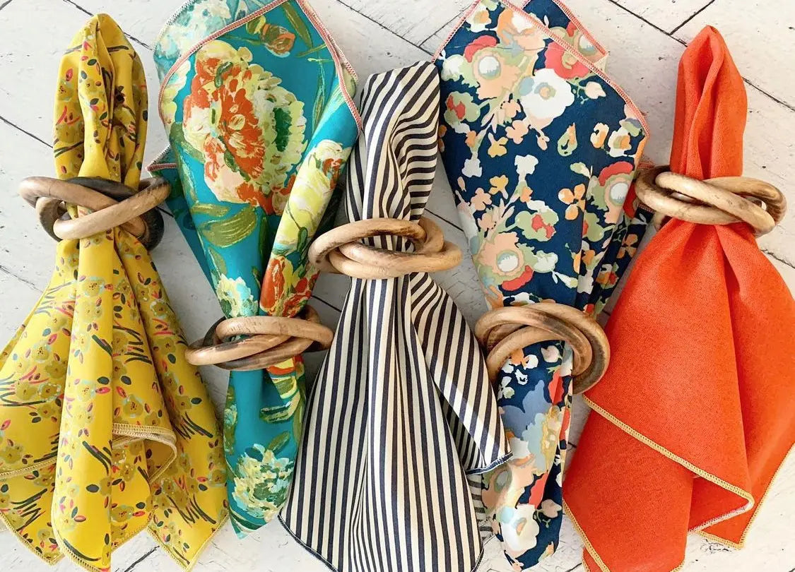 Wood bangles napkin rings holding colorful patterned fabrics and solid orange fabric.