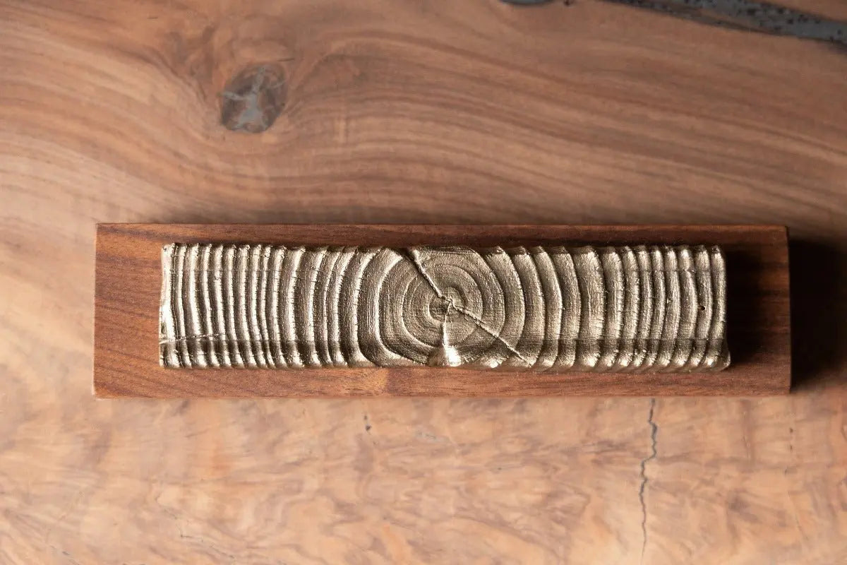 Wooden incense holder with bronze casting of tree rings on a dark wooden base, showcasing its unique design and material.