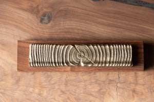 Wooden incense holder with bronze casting of tree rings on a dark wooden base, showcasing its unique design and material.