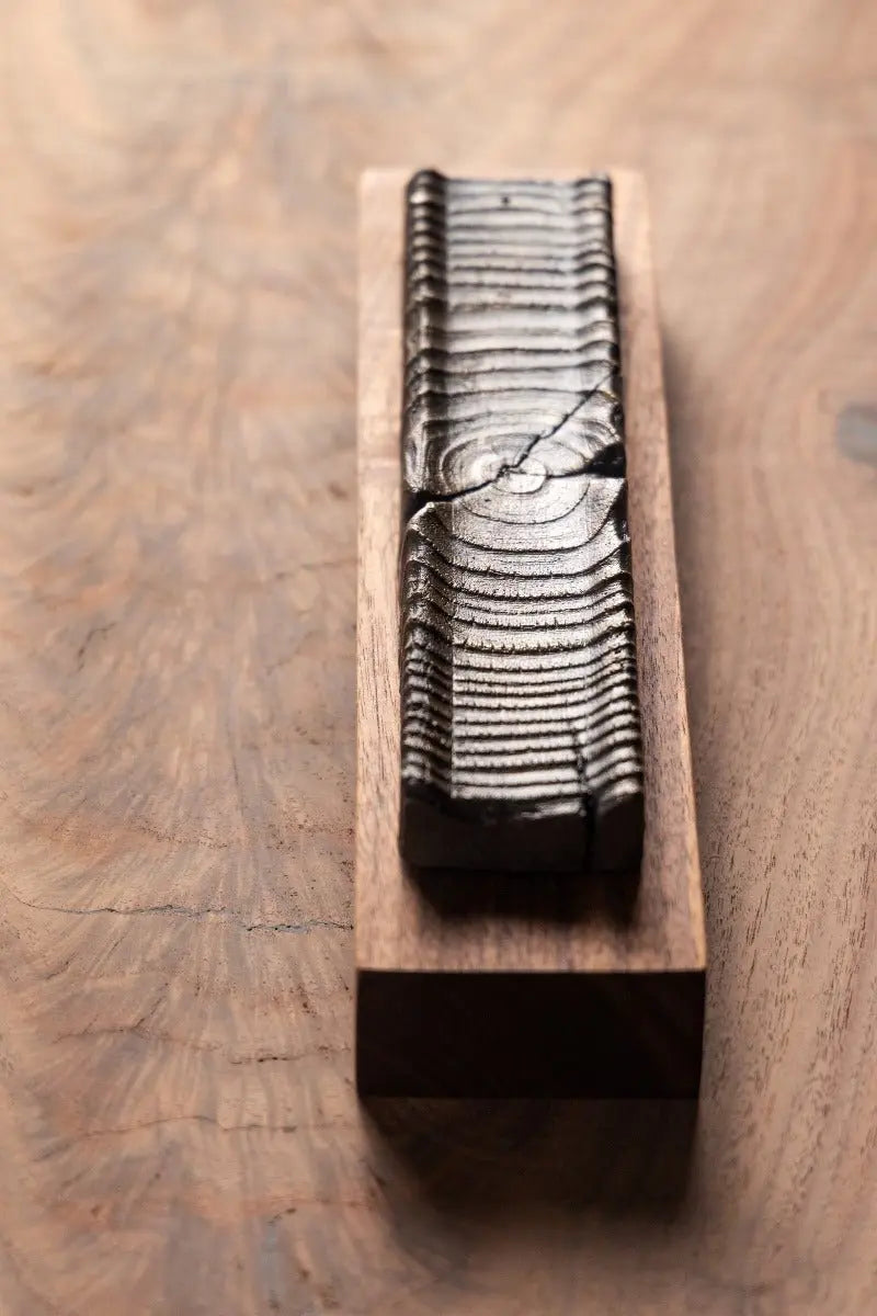 Wooden incense holder with bronze casting on a wood surface showing wood grain.