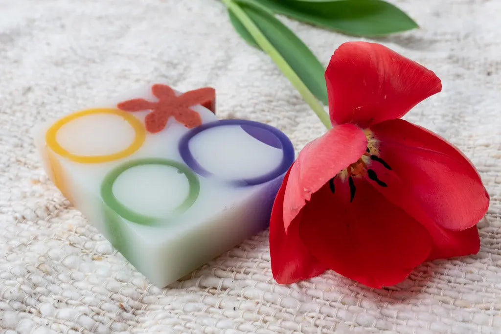 Heart-shaped soap with colorful circles and a red tulip on a textured surface.