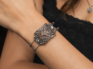 Silver bracelet with intricate design on a wrist against a blurred background