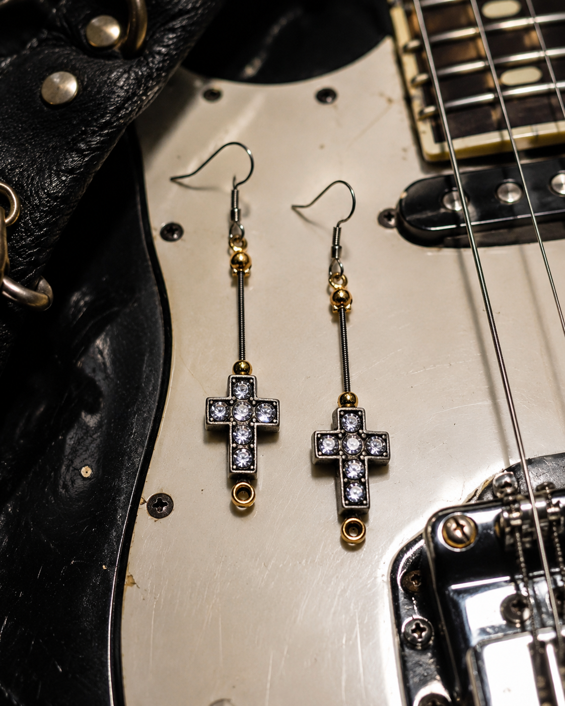 Cross-shaped earrings with clear stones on a guitar body