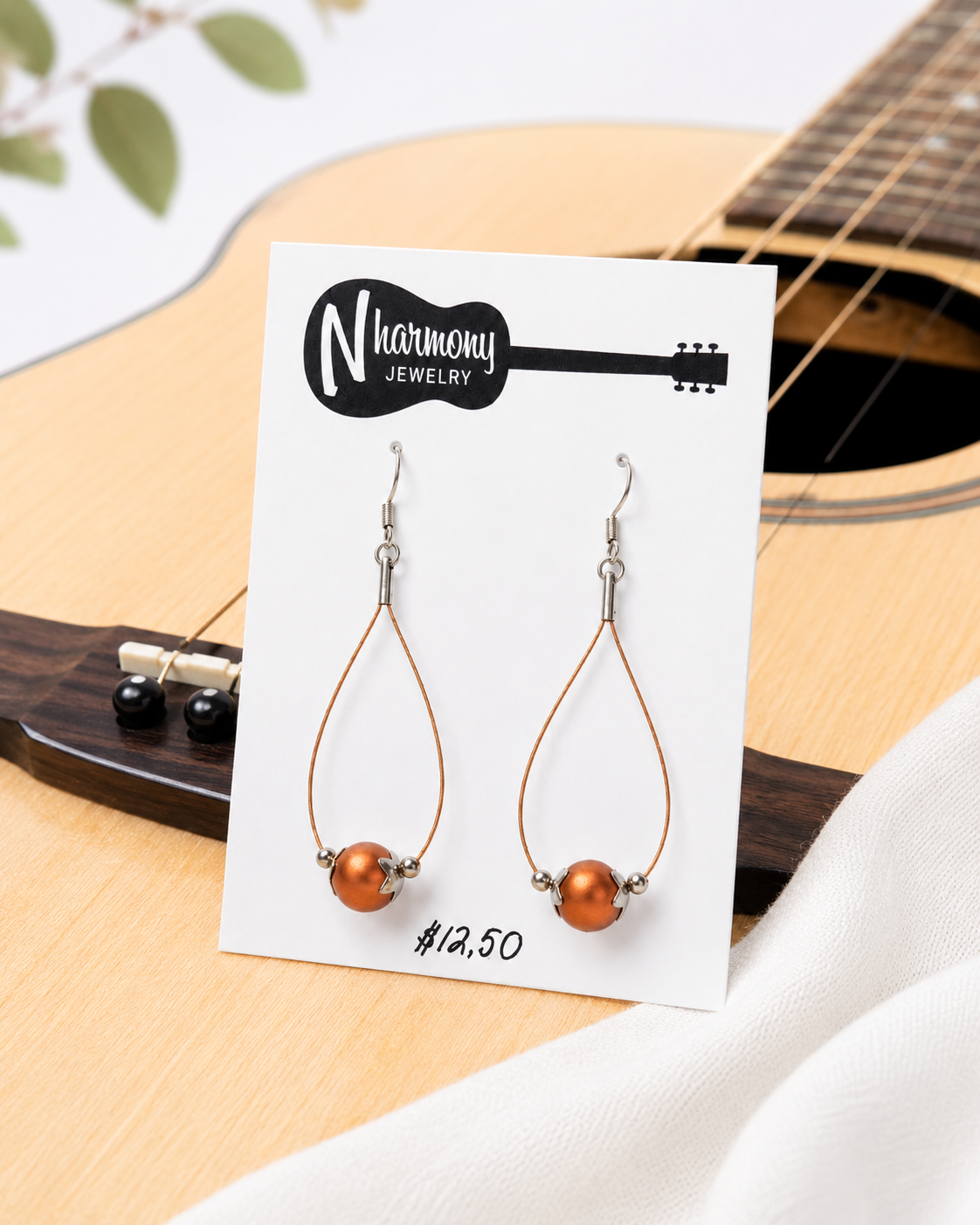 Teardrop-shaped earrings on a 'N Harmony Jewelry' card with a guitar in the background