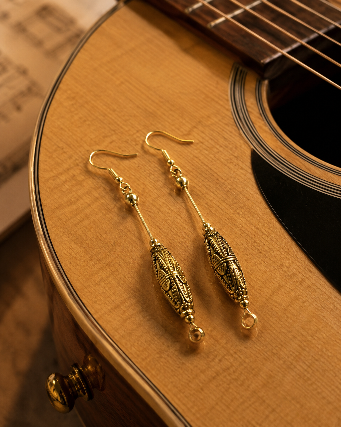 Gold earrings on a wooden surface with a guitar in the background